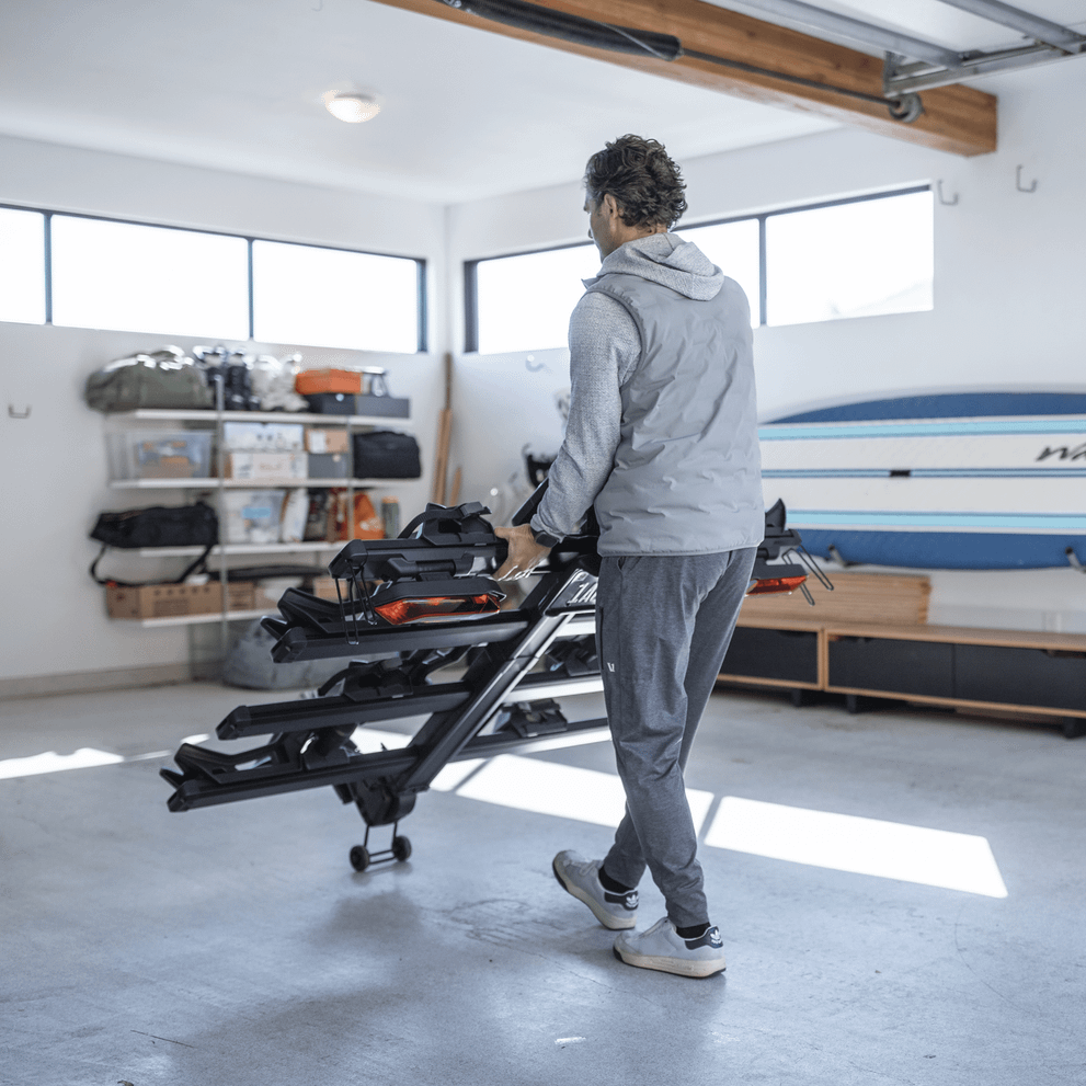A man wheels the Thule Verse hitch bike rack in his garage.