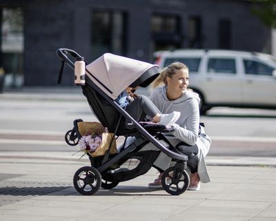 Eine Frau sitzt neben einem rosafarbenen Kinderwagen mit verschiedenem Kinderwagenzubehör.