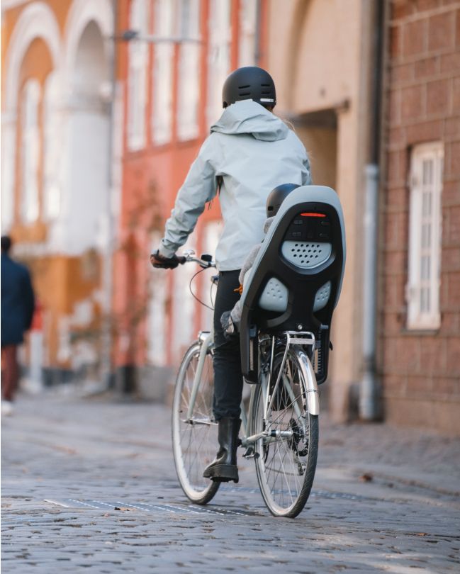 Henkilö ajaa kaupunkiympäristössä polkupyörällä, johon on kiinnitetty polkupyörän Thule Yepp ‑lastenistuin.