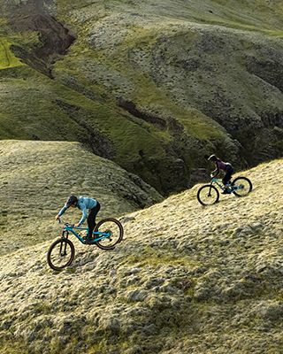 Eine Frau mit einem Thule Vital Trinkblasenrucksack fährt mit dem Fahrrad durch die raue isländische Landschaft.