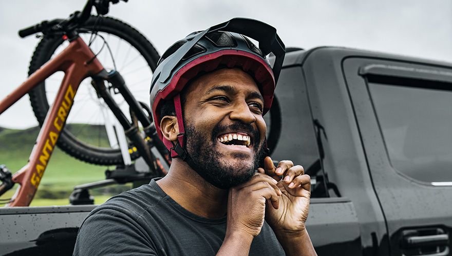 Eliot Jackson prendendo seu capacete com uma picape e um rack para bicicletas para picape Thule com uma bicicleta atrás.