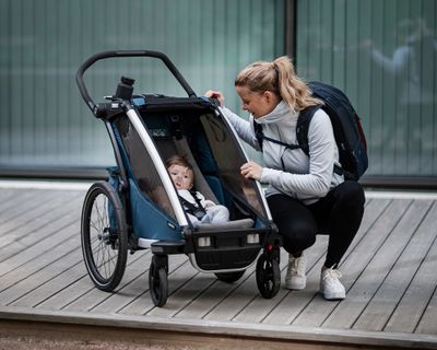 Uma mulher olha para o filho num atrelado para bicicleta e com um acessório de atrelado para bicicleta.