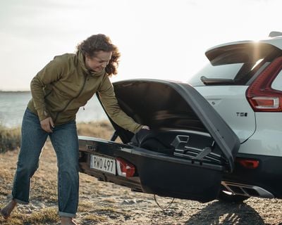 A woman reaches into a rear cargo box and pulls out a cargo duffel.
