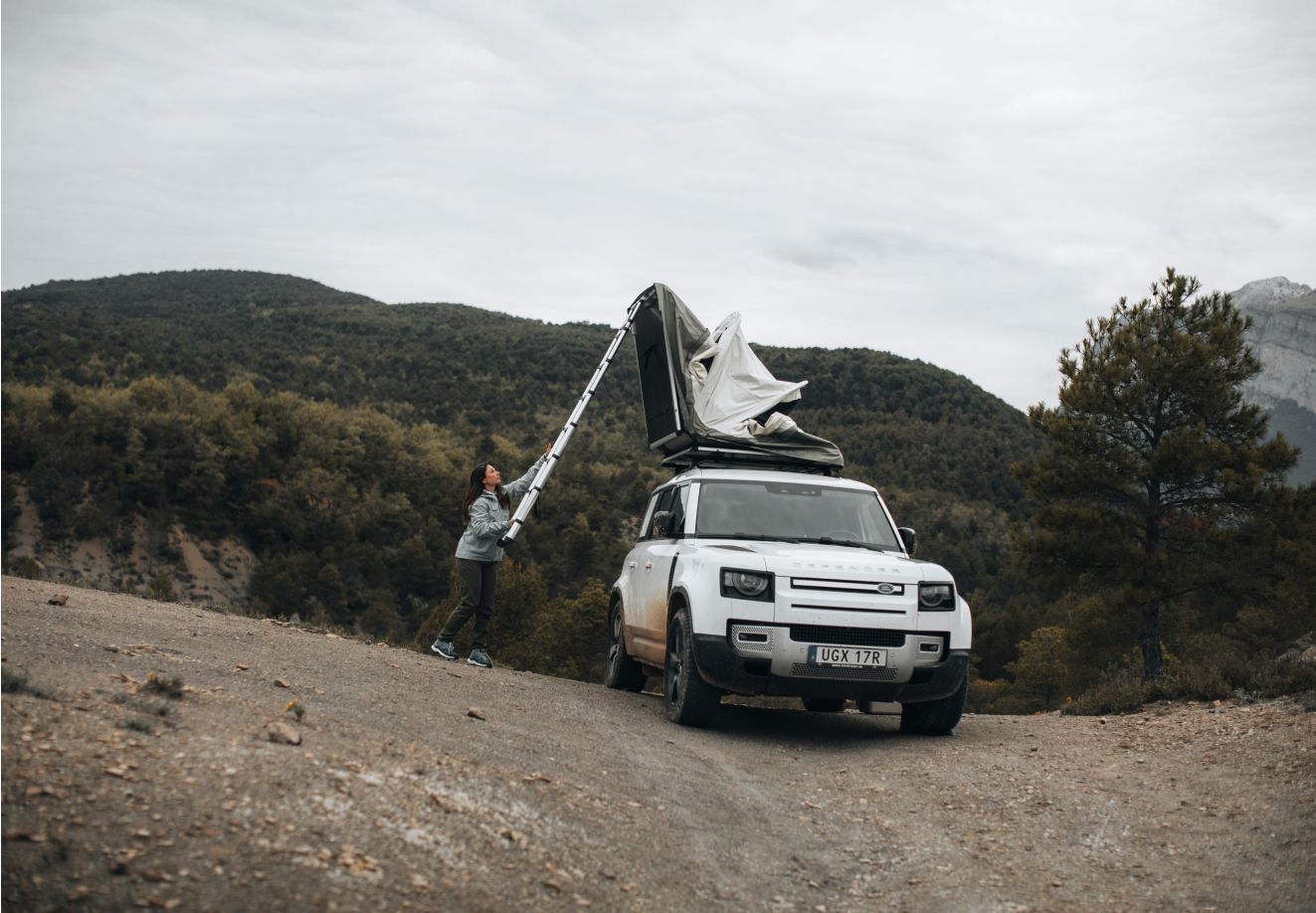 A person unfolding a Thule Approach rooftop tent while parked on a mountain road.