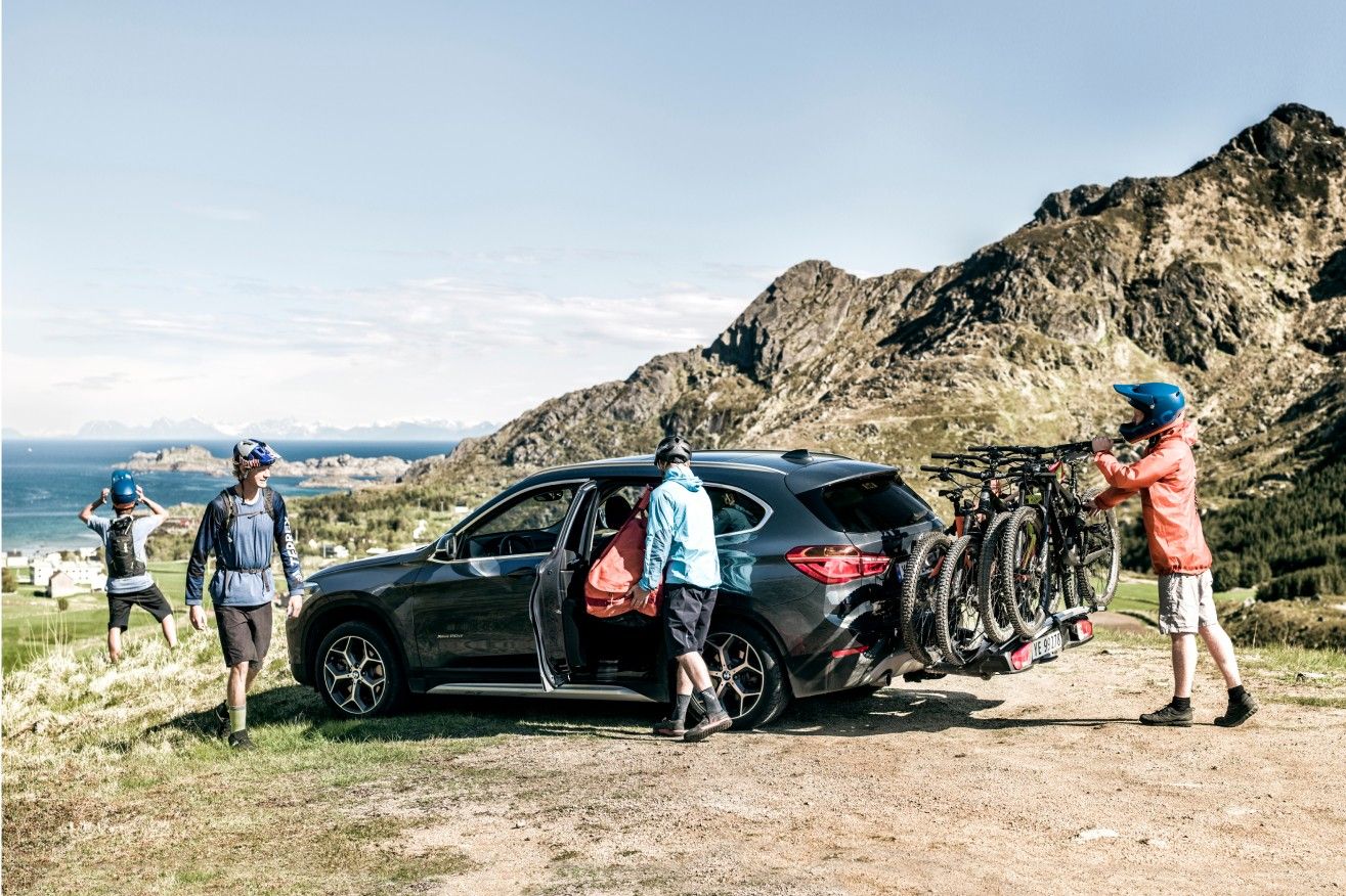 A car is parked in the rocky mountains with a towbar bike rack and people walking towards the vehicle.